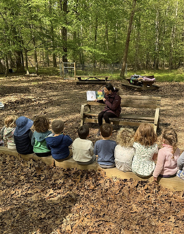 Outdoor storytime with young children gathered around a reader, building confidence and social connection through shared storytelling.